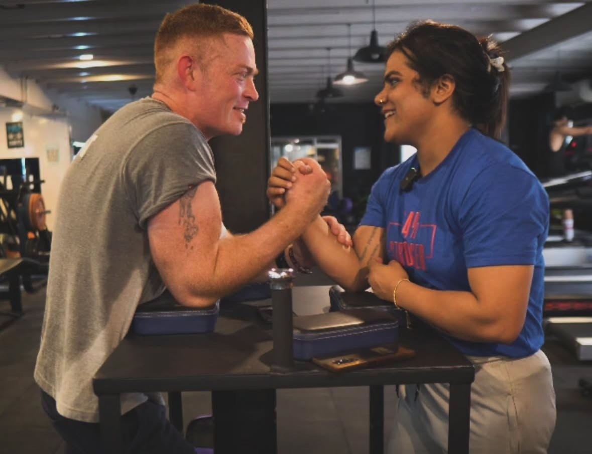 Ryan and Chetna smiling at each other across an armwrestling table in the gym